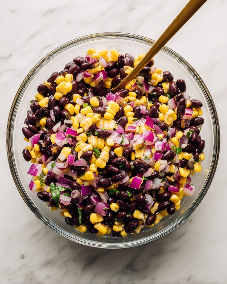 A clear glass bowl sits on a white marbled surface, filled with three main layers of food: shiny black beans, bright yellow corn kernels, and small pieces of purple and white onion. These ingredients are mixed together in a colorful, chunky salad texture. A long gold spoon is placed inside the bowl, slightly resting on the edge. The photo is taken from above, showing all the layers clearly. photo taken with an iphone --ar 4:5 --v 7