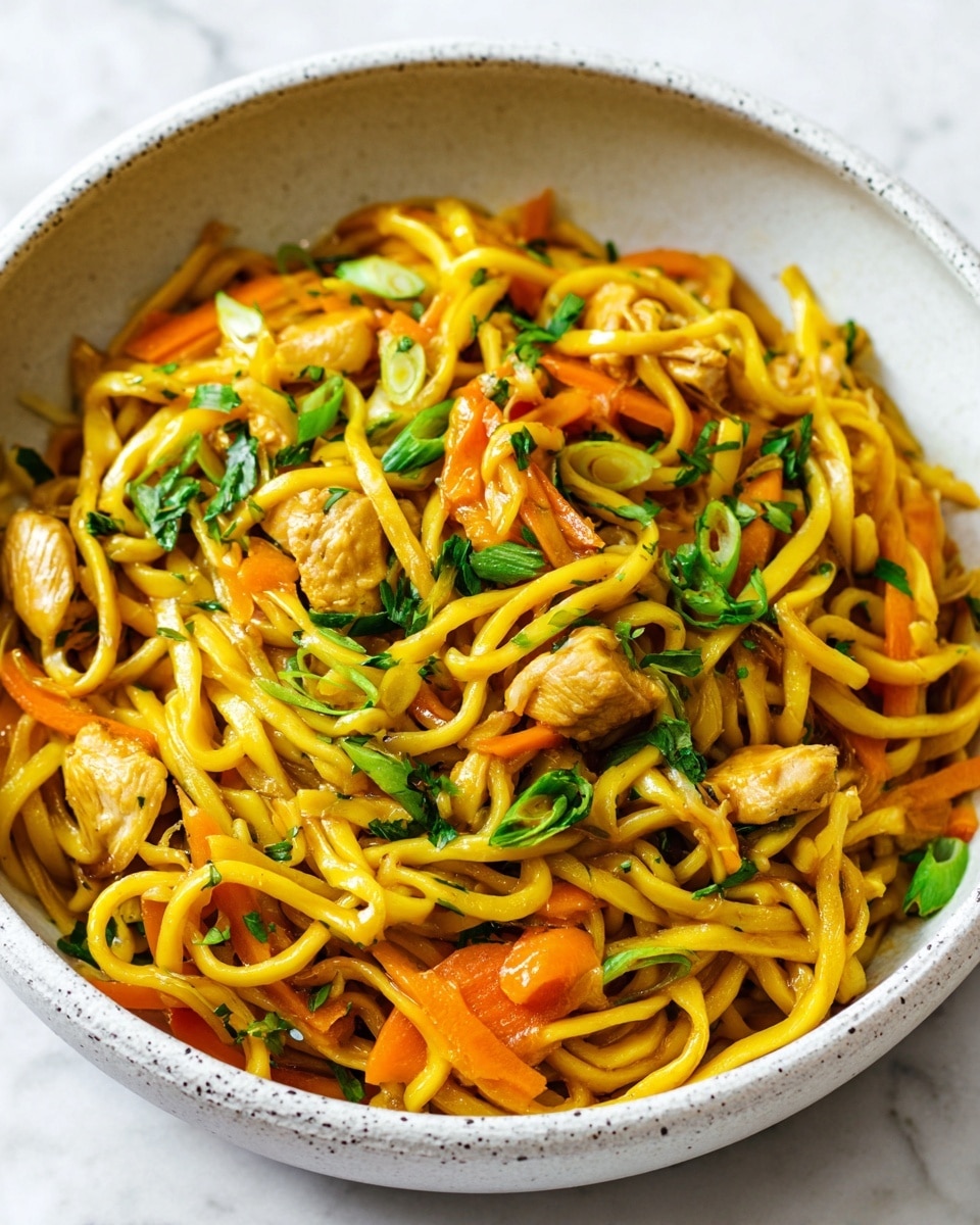 A bowl filled with thick, glossy yellow noodles mixed with small pieces of light brown cooked chicken and slices of orange carrot. Green onion slices and fresh green herbs are scattered on top, adding bright green color. The noodles appear soft and shiny, mixed evenly with the vegetables and chicken, in a white bowl with a speckled inner surface, placed on a white marbled background. photo taken with an iphone --ar 4:5 --v 7