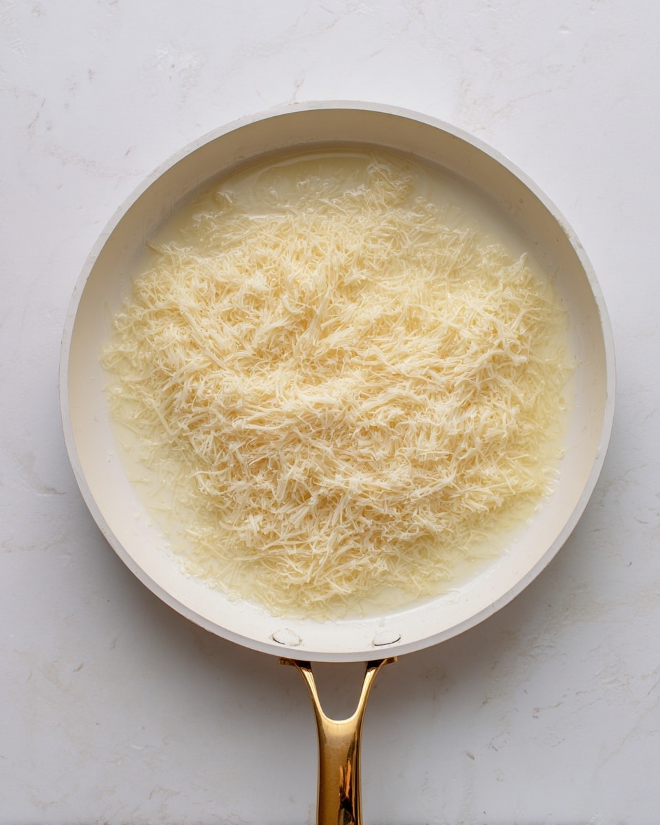 A white pan with a gold handle is shown from above, filled with a thin layer of melted butter on the bottom. On top of the butter, there is a large, even layer of fine, pale yellow shredded strands, spread mostly flat but with some subtle texture. The pan rests on a white marbled surface, with soft lighting enhancing the light colors and delicate textures. photo taken with an iphone --ar 4:5 --v 7